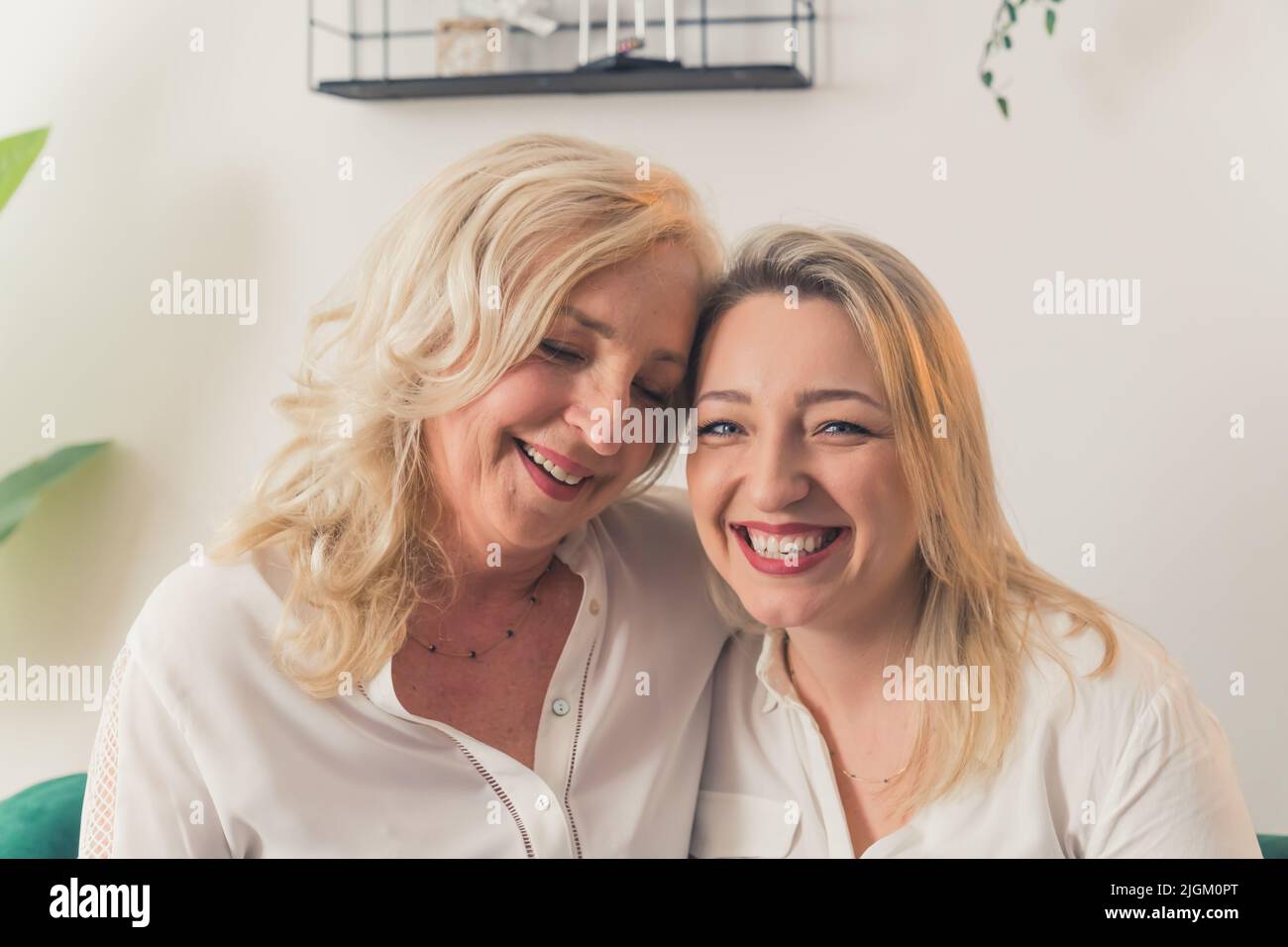 Due donne bionde che guardano allo stesso modo, indossando eleganti camicie bianche, guardando direttamente una macchina fotografica. Femmine che si guardano l'un l'altro con amore e allegria. Foto di alta qualità Foto Stock