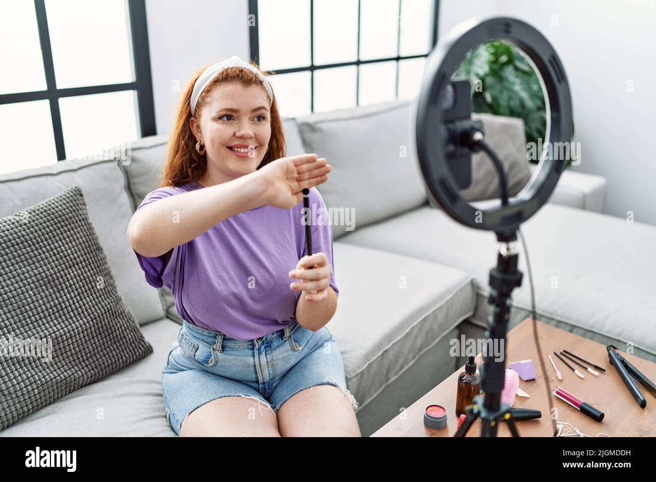 Giovane donna rossa che fa un tutorial sul trucco con smartphone a casa Foto Stock