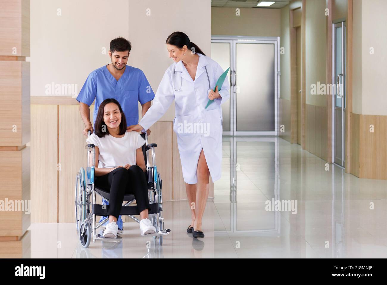 felice sorridente paziente asiatico donna seduta in sedia a rotelle con infermiera maschio parlare con il medico dopo il recupero dal piano di trattamento chirurgico in ospedale Foto Stock