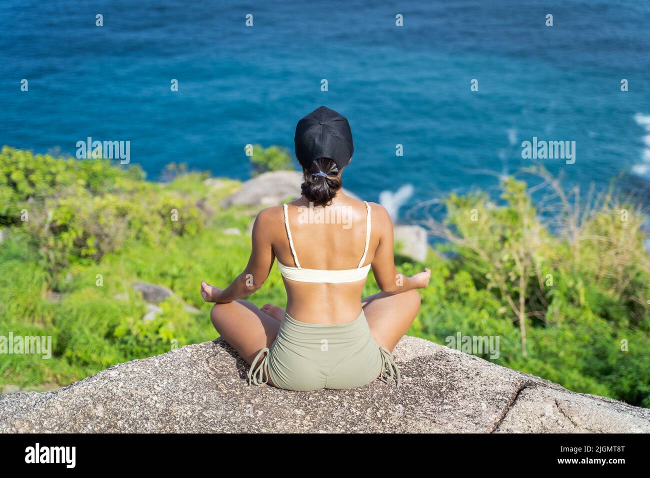 Dorso di giovane donna asiatica meditating sulla scogliera di montagna con una vista del mare. Bella femmina che si allenano all'aperto Foto Stock