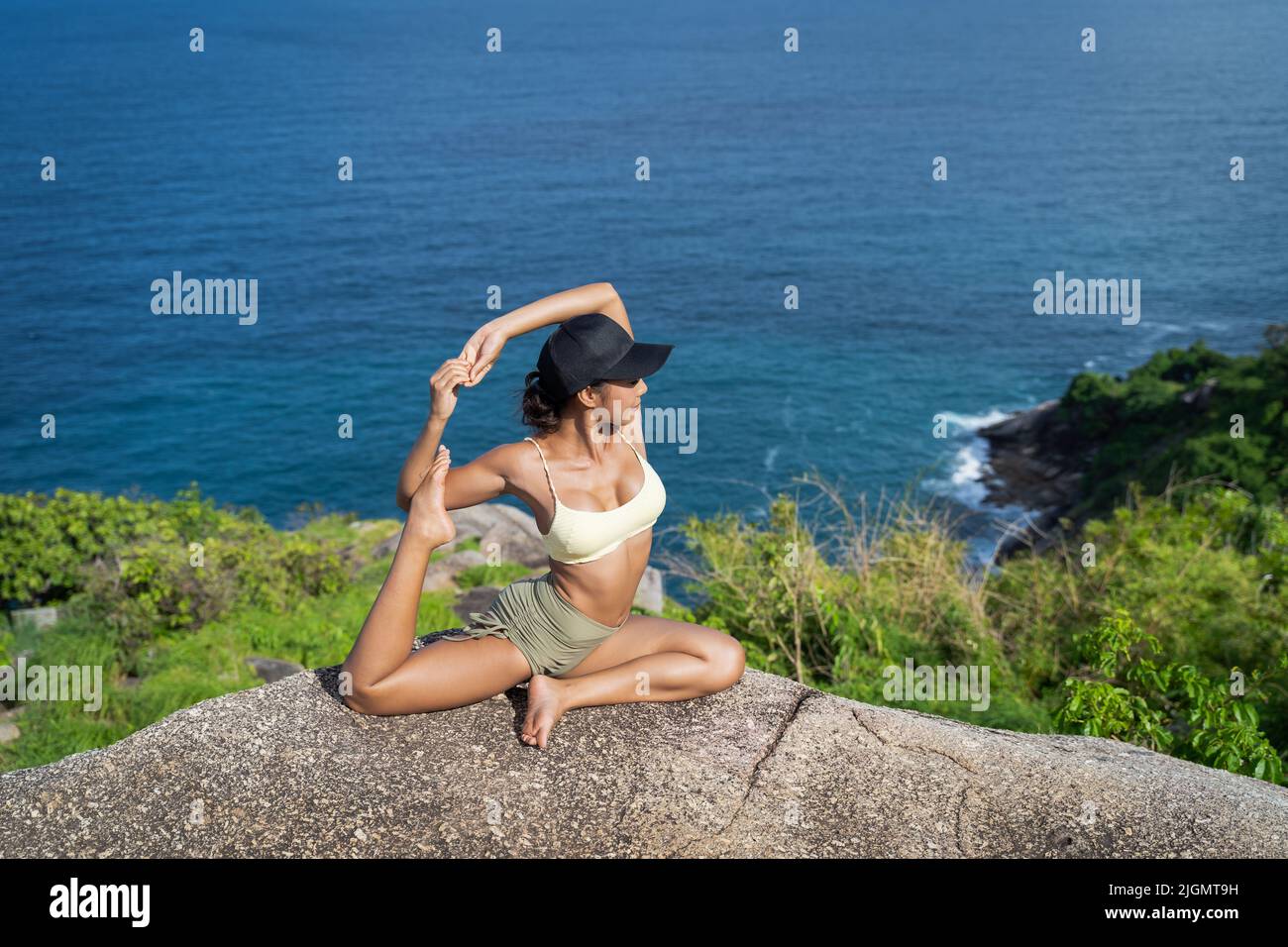 Giovane donna asiatica che pratica yoga sulla scogliera di montagna con vista mare. Bella femmina che si allenano all'aperto nella natura Foto Stock