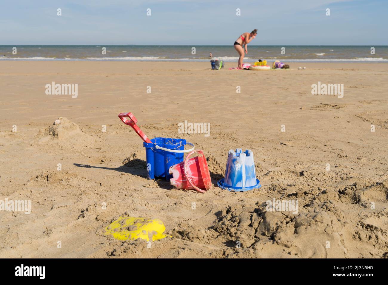 Una donna che prende il sole sulla spiaggia sabbiosa, con secchi blu, rossi e gialli e set di vanga , Kent Inghilterra uk Foto Stock
