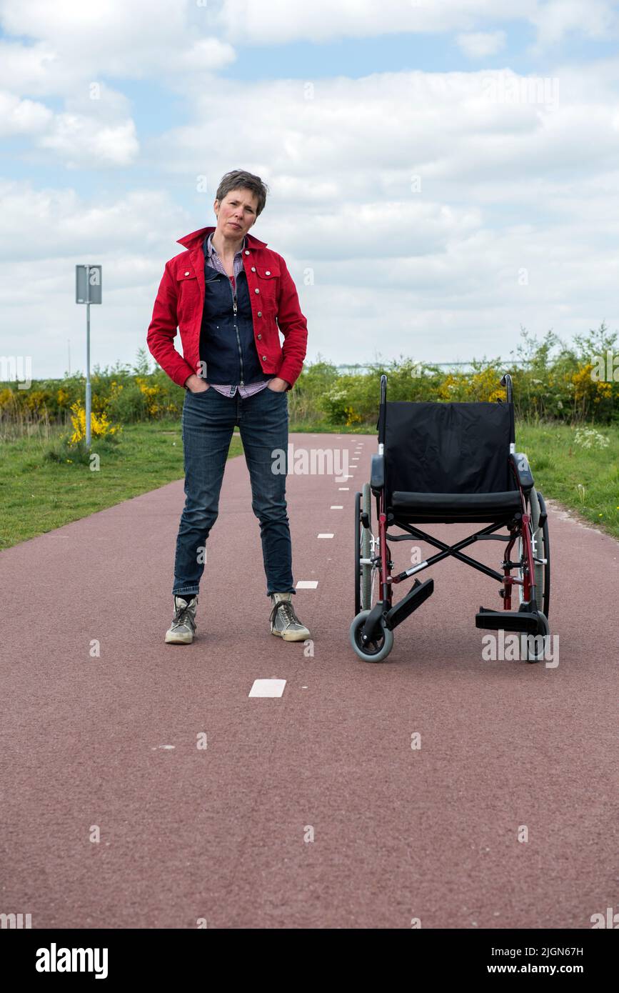 Tilburg, Paesi Bassi. Matura donna aldult sofferenza forma MS / Sclerosi multipla a piedi il suo percorso oltre la sua sedia a rotelle. Foto Stock