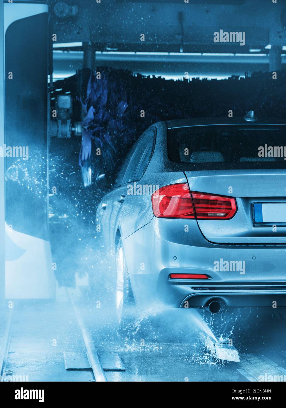 Un'auto grigia che attraversa un autolavaggio automatico con spazzole e acqua che colpiscono il veicolo. Foto Stock