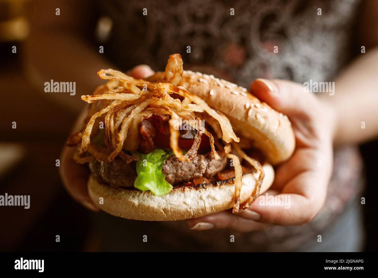 Hamburger gustoso con cipolle in mani femminili Foto Stock