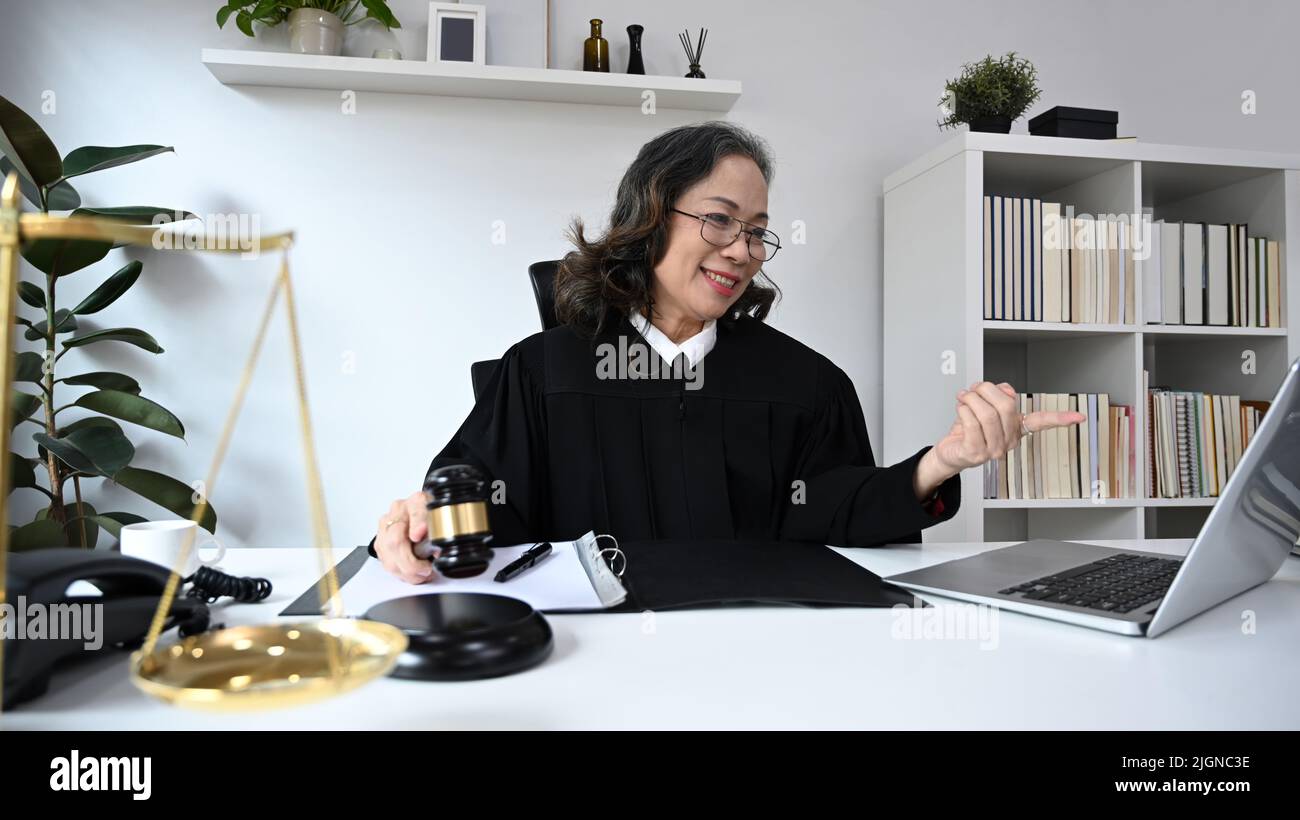Avvocato femminile maturo in abito uniforme seduta davanti al portatile, fornendo la consultazione di legge e consulenza legale online Foto Stock