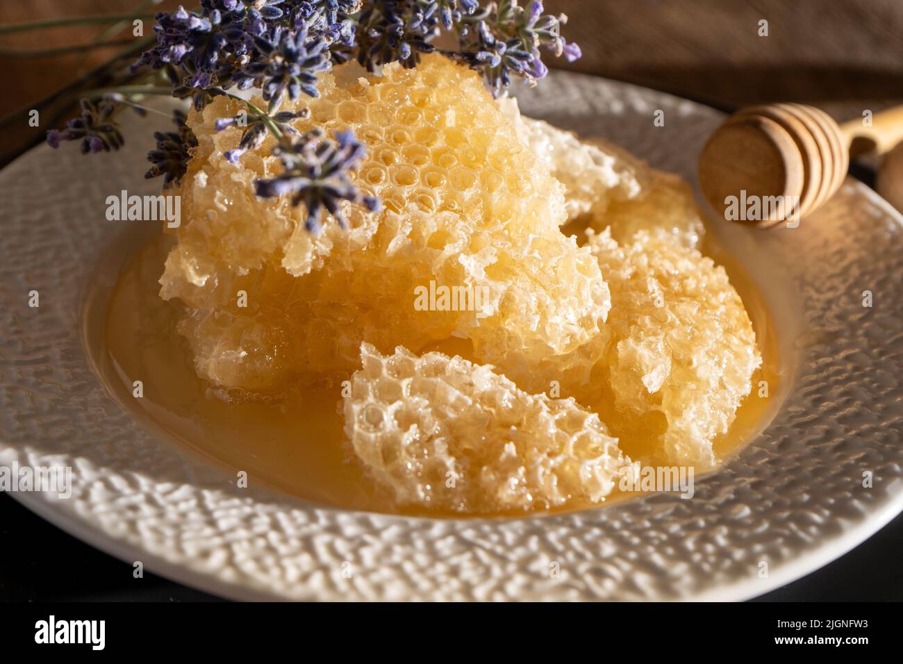 Miele e nido d'ape su un piatto bianco. Cibo dolce in una ciotola sul tavolo. Un prodotto dell'apicoltura. Fiore di lavanda. Foto Stock