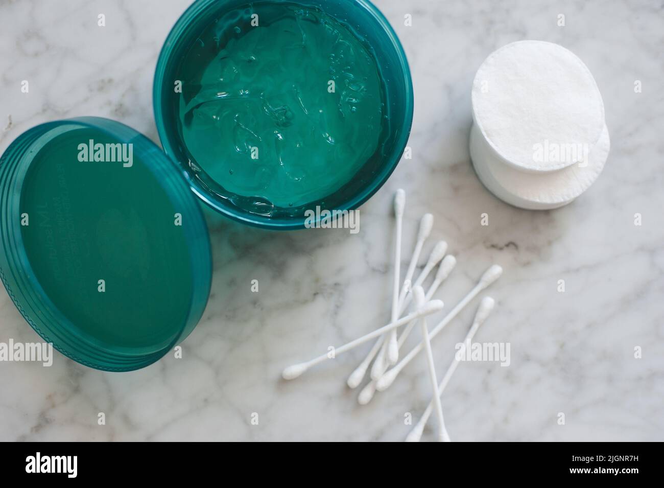 Maschera facciale in gel idratante in vasetto di plastica con tamponi in cotone e bastoni sul tavolo in marmo vista dall'alto. Prodotti di bellezza a casa. Foto Stock