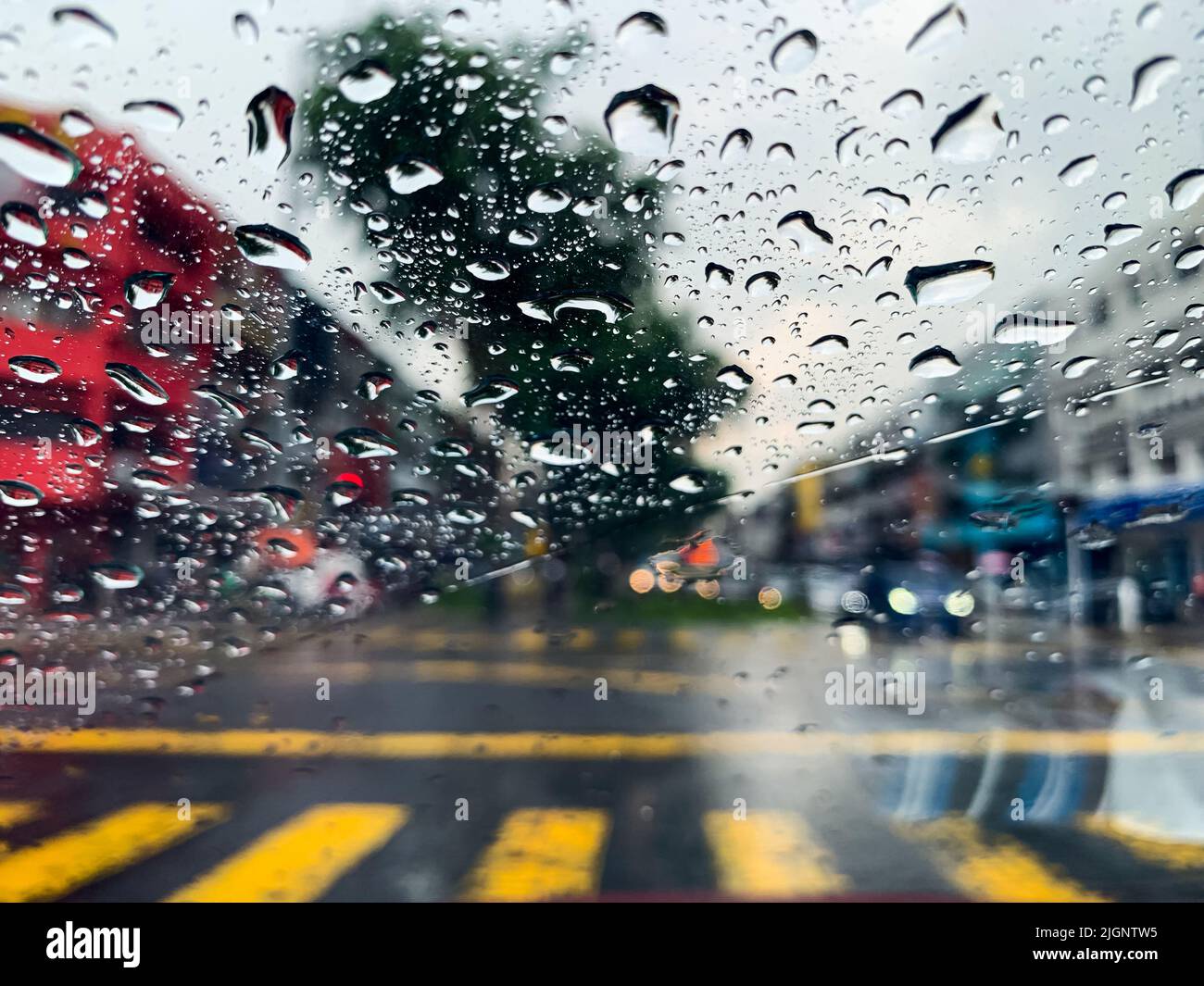 Fuoco selettivo alla goccia d'acqua sul vetro dell'automobile quando piove alla stagione monsonica con sfondo sfocato della strada. Foto Stock