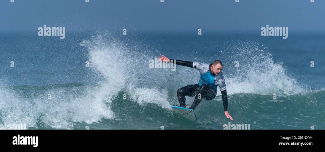 Un'immagine panoramica di un surfista maschile che gareggia in una gara di surf al Fistral di Newquay in Cornovaglia nel Regno Unito. Foto Stock
