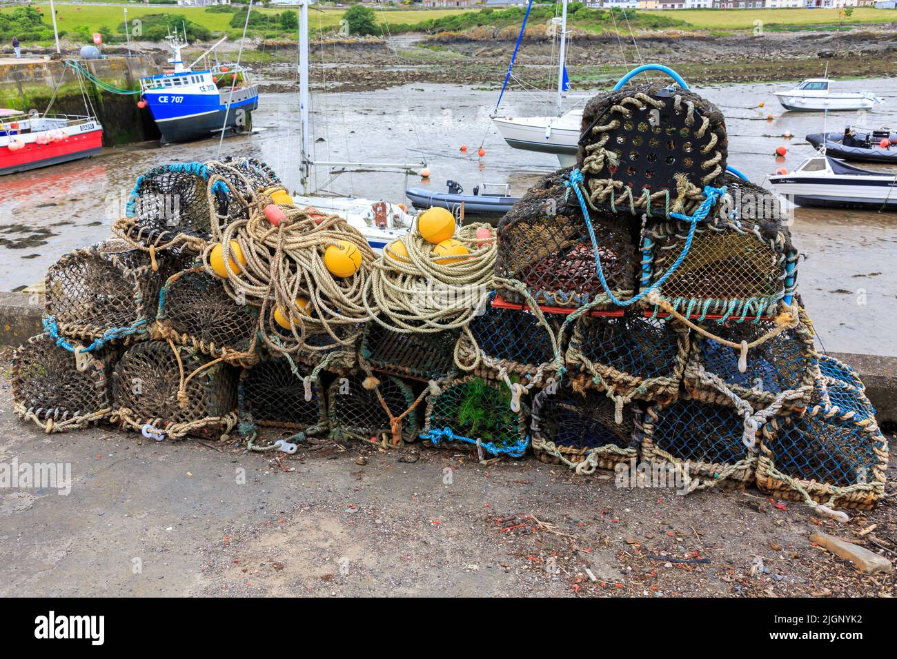 L'isola di Whithorn, Scozia - 13 giugno 2022: Vasi di aragosta, Galleggianti e funi accatastati sulla parete del porto con il porto sullo sfondo basso Foto Stock