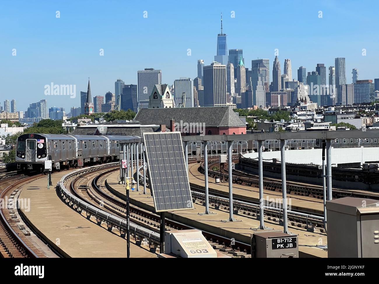 F linea ferroviaria che arriva alla stazione metropolitana di Smith Ninth Street con una vista chiara dello skyline di Lower Manhattan. Foto Stock