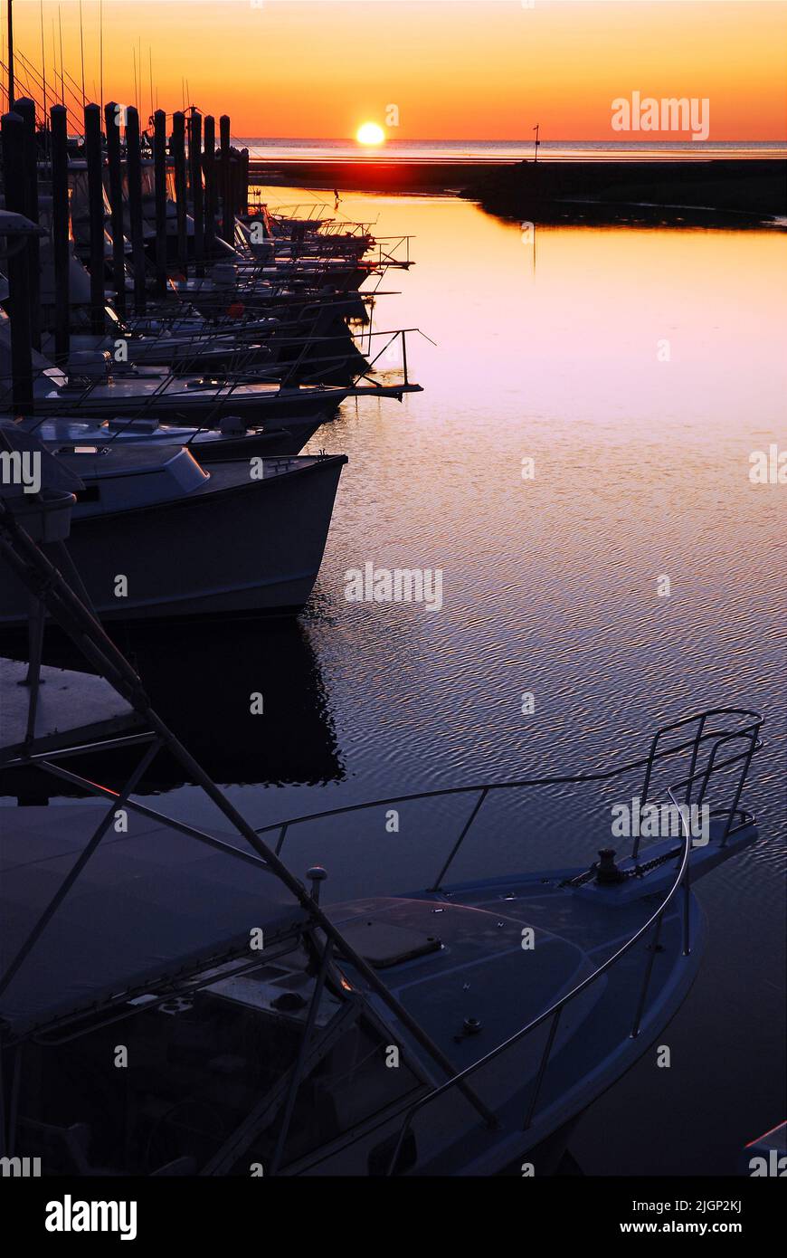 Il cielo del tramonto e il sole si riflettono nelle acque ferme di un porto con le barche e le navi ormeggiate al molo del porto turistico di Cape Cod Foto Stock
