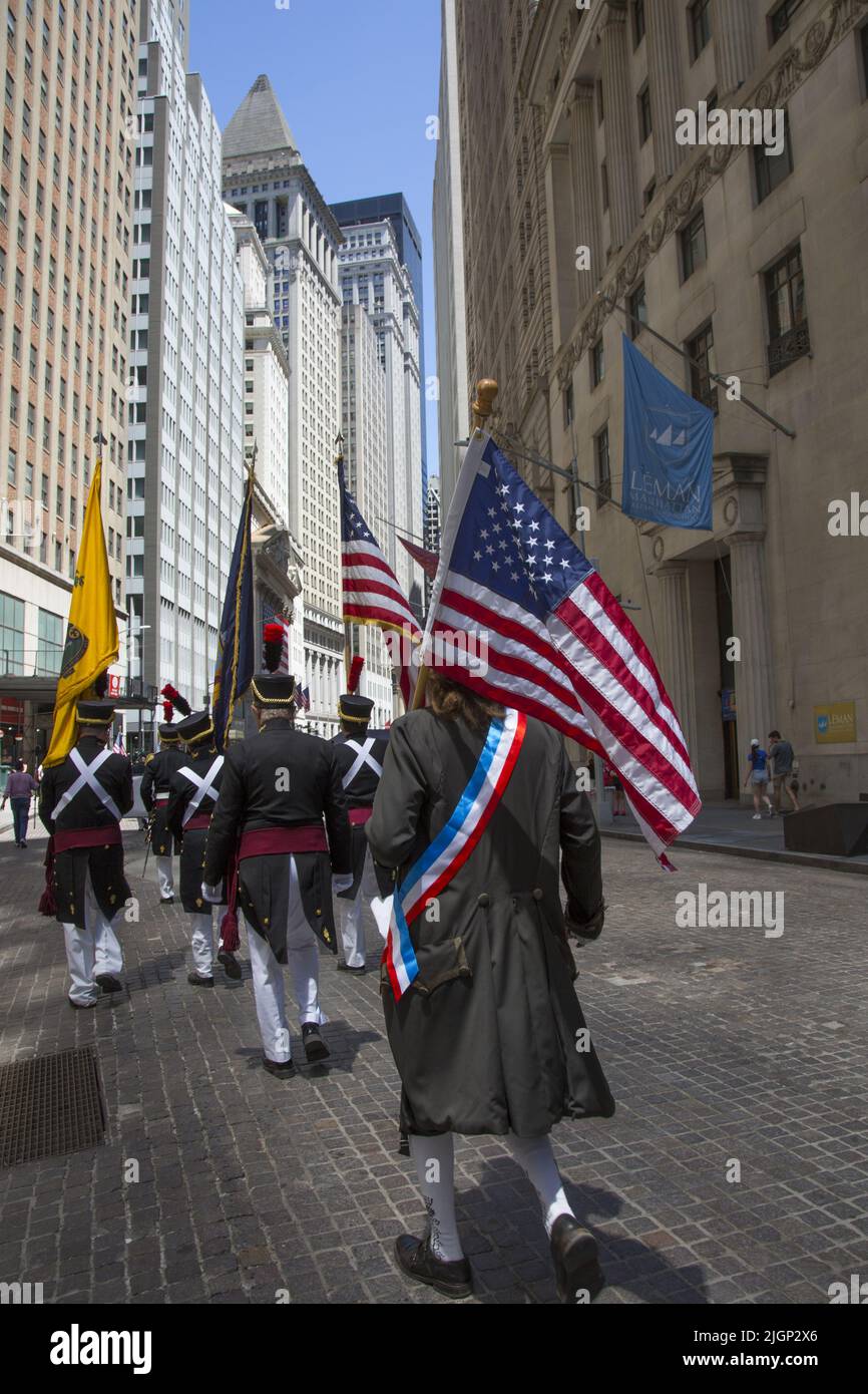 Gli uomini con bandiere americane che indossano uniformi della guerra rivoluzionaria marciano su Broad Street nello storico quartiere finanziario di Lower Manhattan il giorno dell'Indipendenza, luglio 4th. Foto Stock