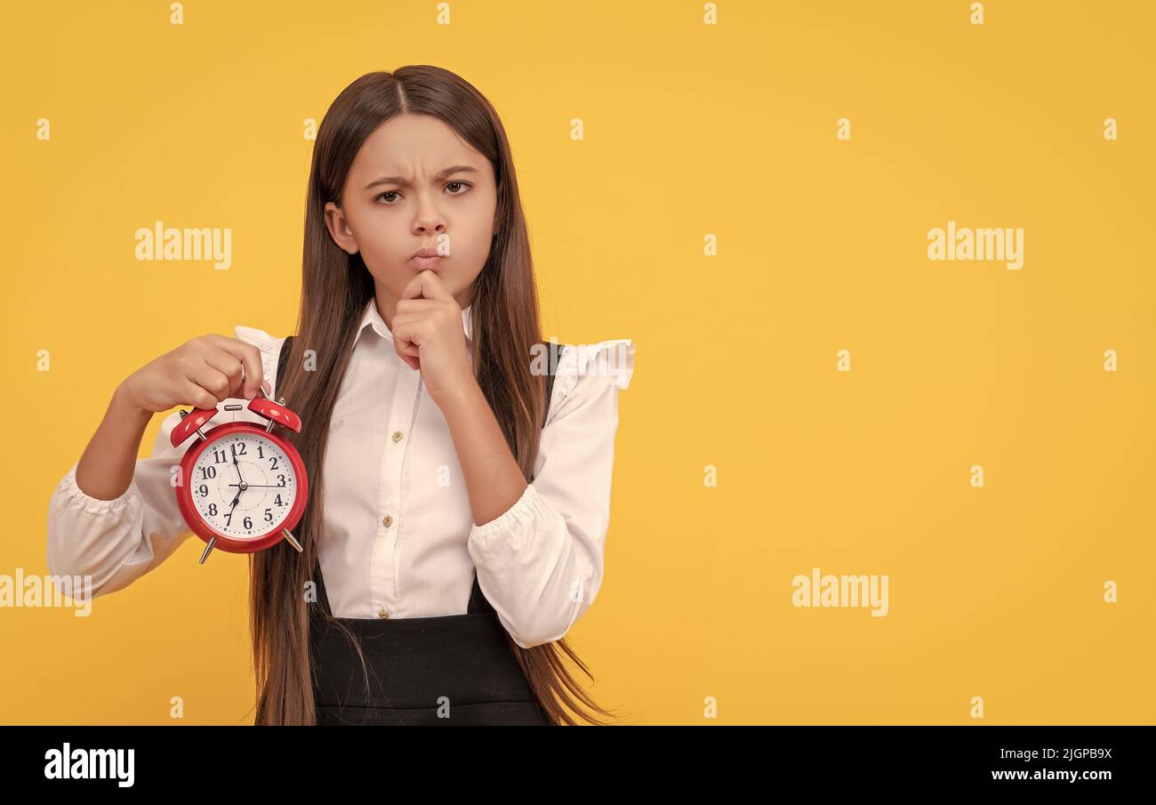 il bambino ponderante con la sveglia. il bambino della scuola in uniforme mostra il tempo. siete in ritardo. Foto Stock