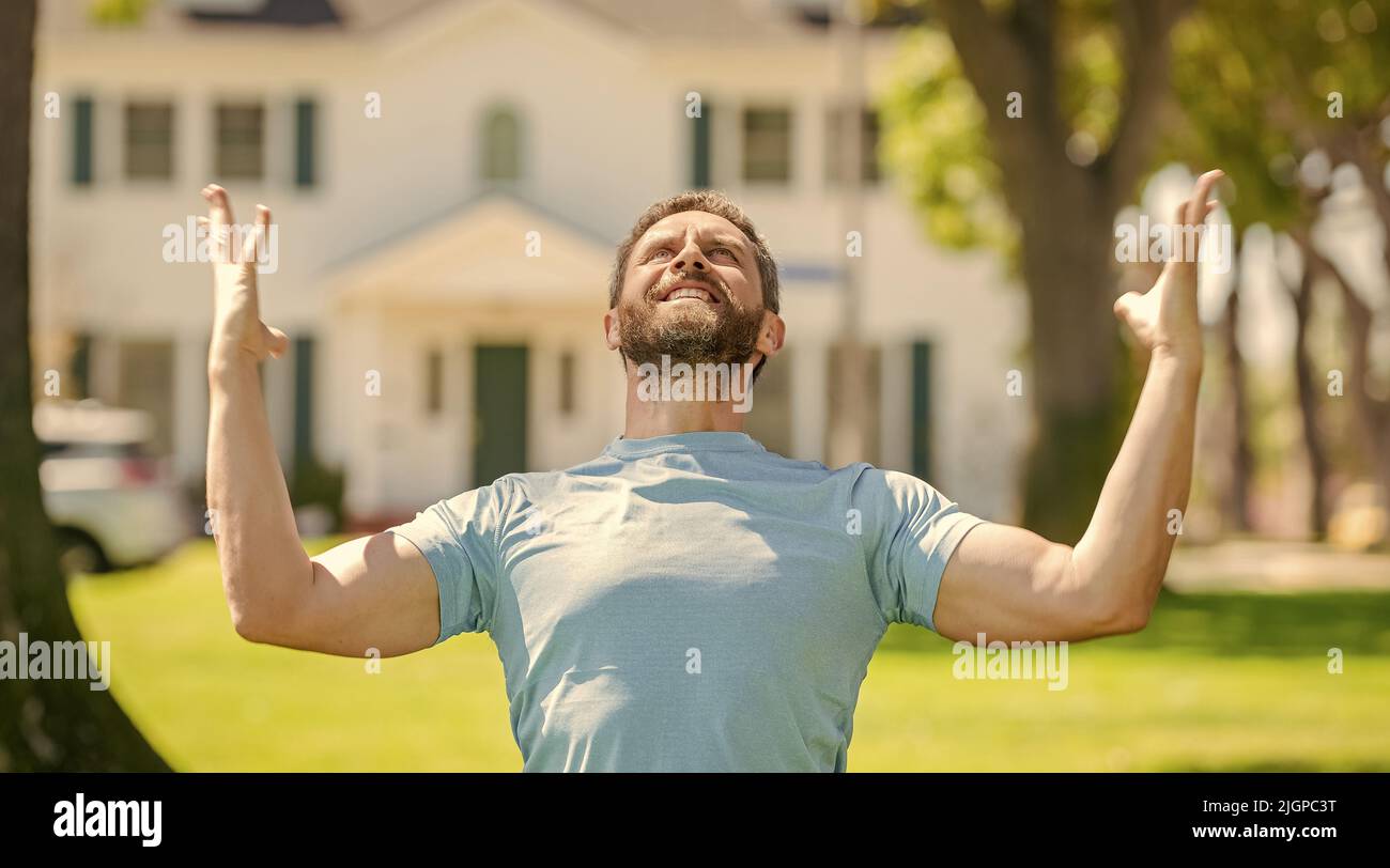 felice unshaven ragazzo in piedi vicino casa nuova celebrando il successo, nuova casa Foto Stock