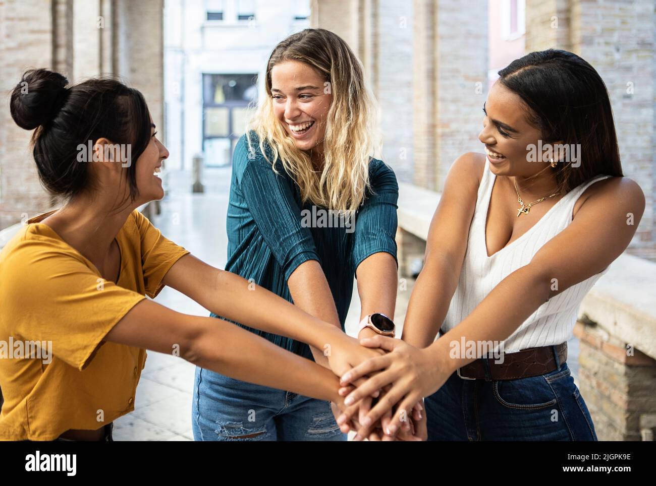 Tre giovani amici multietnici uniti che si accatastano le mani all'aperto Foto Stock