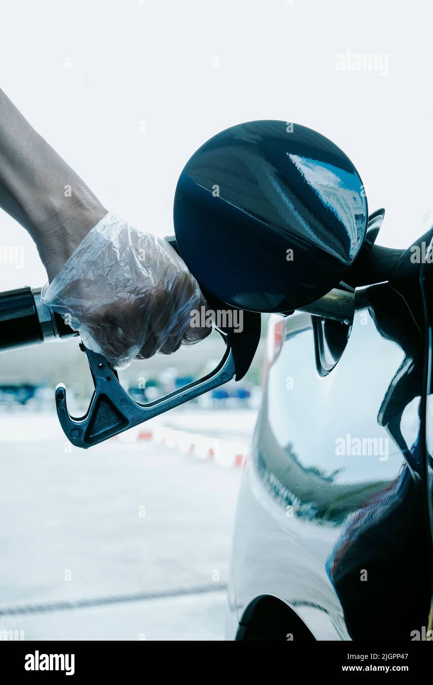 un giovane uomo caucasico, indossando guanti di plastica, riempie il serbatoio del carburante dell'auto in una stazione di servizio Foto Stock