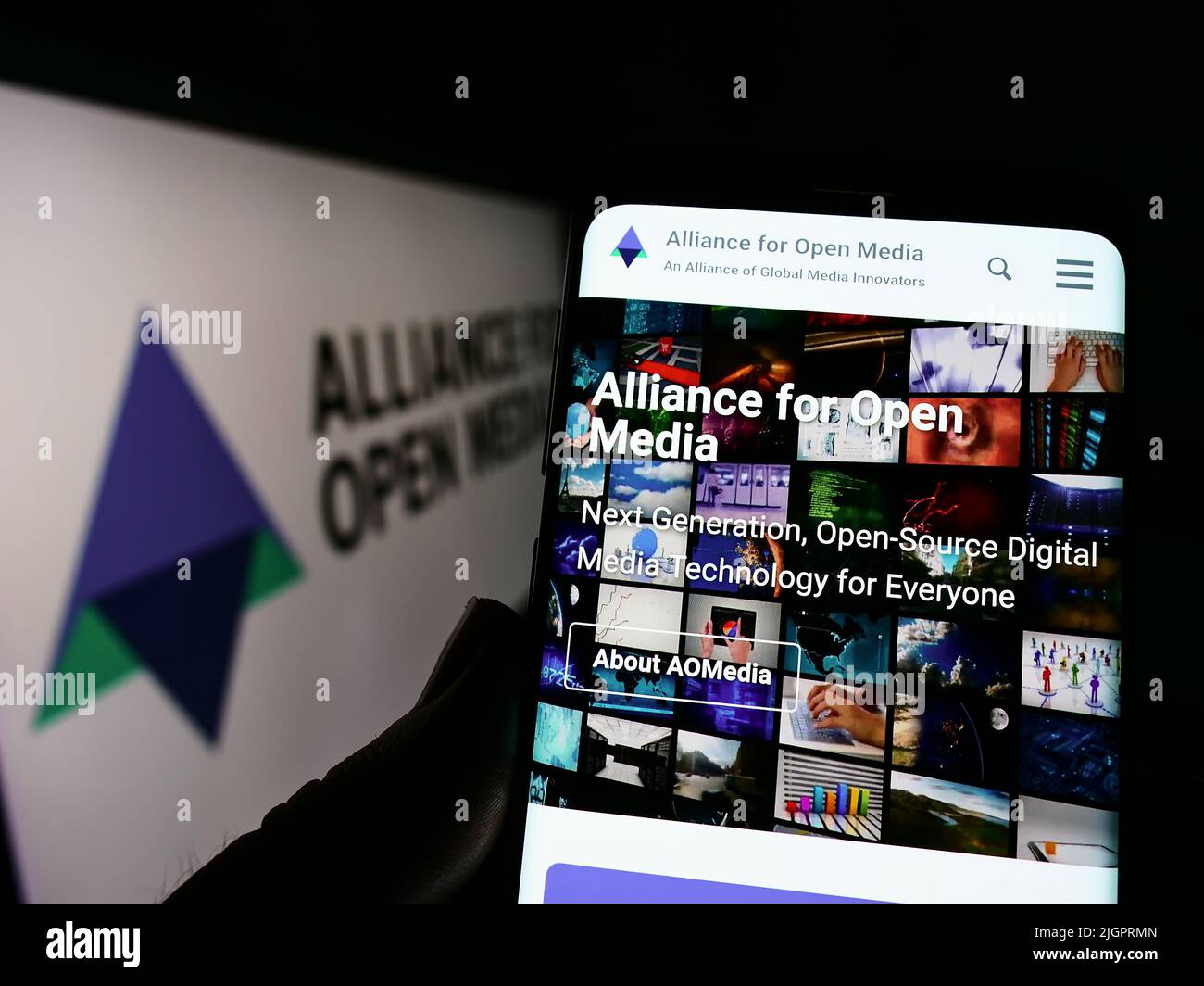 Persona che detiene il cellulare con il sito web di Consorzio Alliance for Open Media (AOMedia) su schermo con il logo. Concentrarsi sul centro del display del telefono. Foto Stock