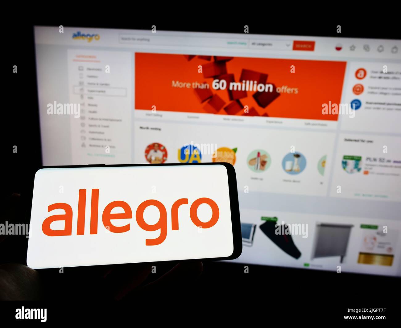 Persona che detiene il cellulare con il logo della società polacca di e-commerce Allegro.pl Sp. z o. o. o. sullo schermo di fronte al sito web. Mettere a fuoco sul display del telefono. Foto Stock