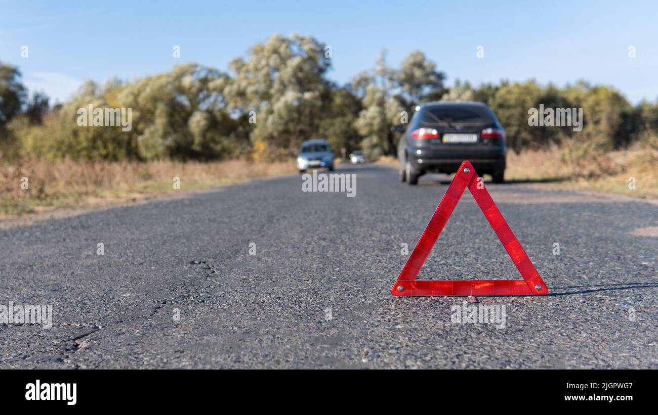 Il triangolo di emergenza si trova sulla strada di fronte alle auto sullo sfondo. Guasto della vettura in tempo di sole. Sicurezza del traffico stradale Foto Stock