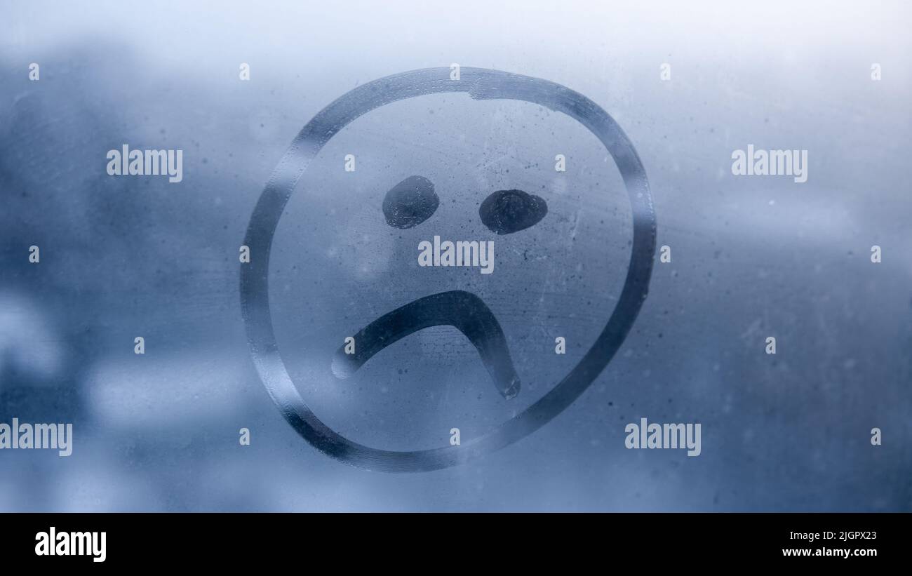 Emoji tristi disegnate a mano sullo sfondo della finestra di vetro appannato. Primo piano del cartello con il volto infelice. Messa a fuoco selettiva sulla foto. Concetto di depressione e tristezza. Foto Stock