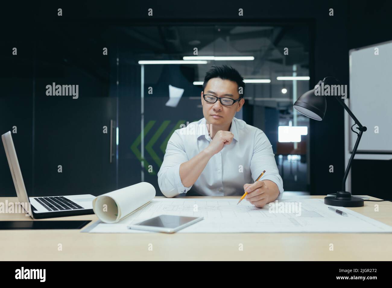 Pensare architetto ingegnere asiatico che lavora in un moderno ufficio di design, uomo che guarda il disegno piano. Foto Stock
