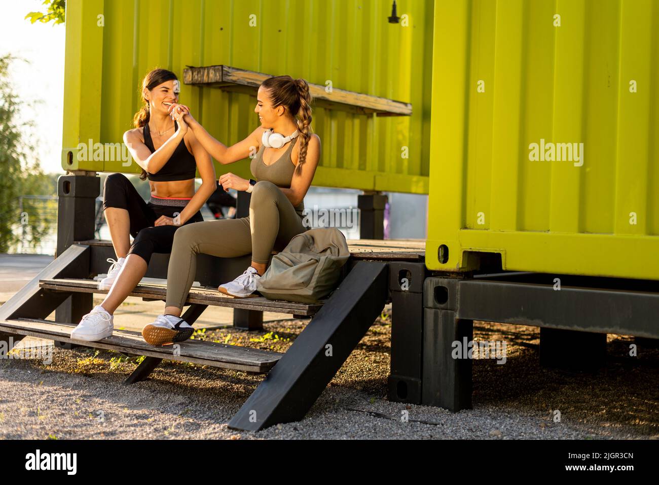 Donne piuttosto giovani in abbigliamento sportivo che si riposano dopo l'esercizio su una passeggiata sul fiume Foto Stock