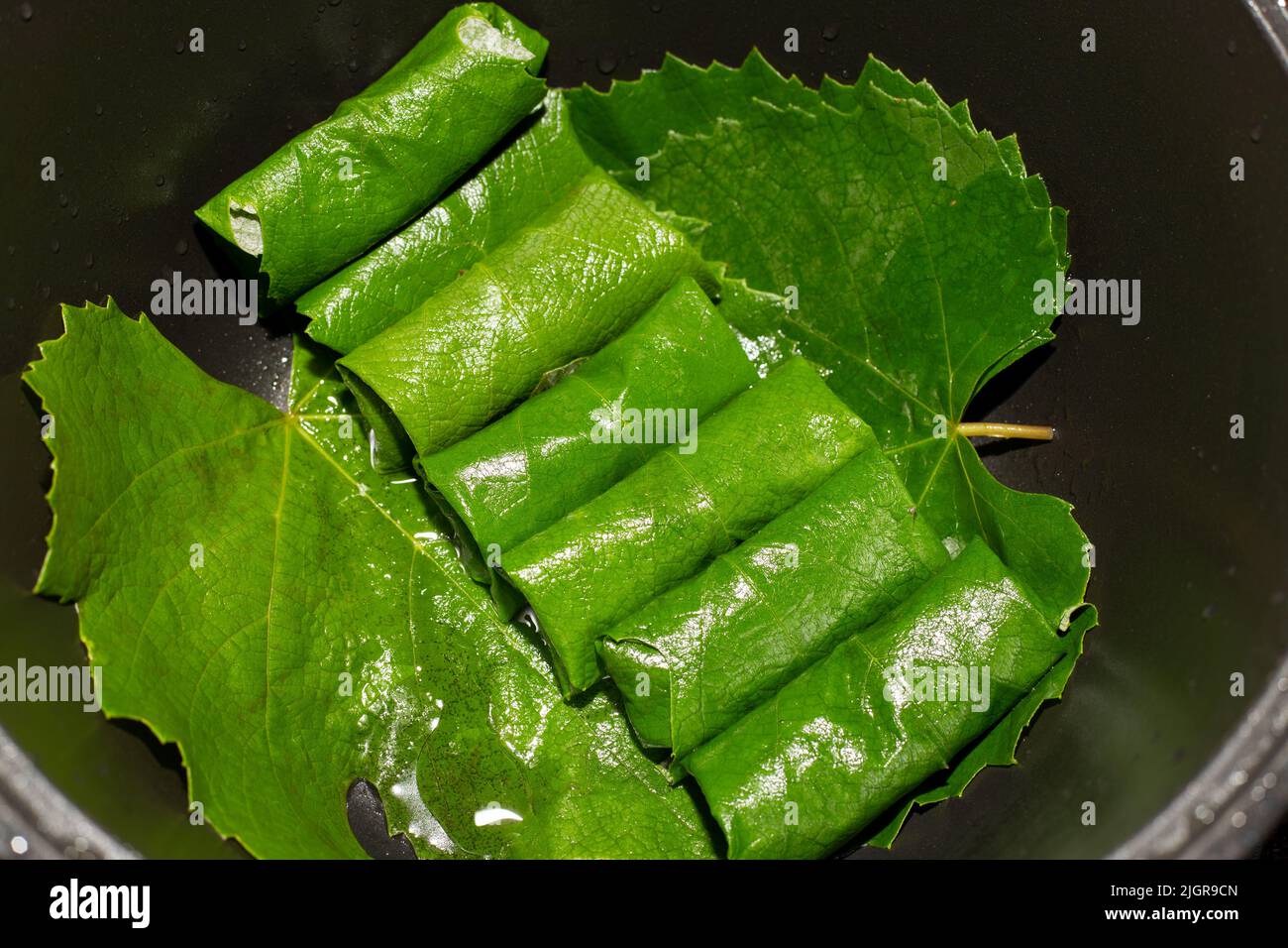 Carne macinata avvolta in foglie d'uva - piatto di dolma caucasica in un cavoldro di ghisa nera. Cucinare a casa. Foto Stock