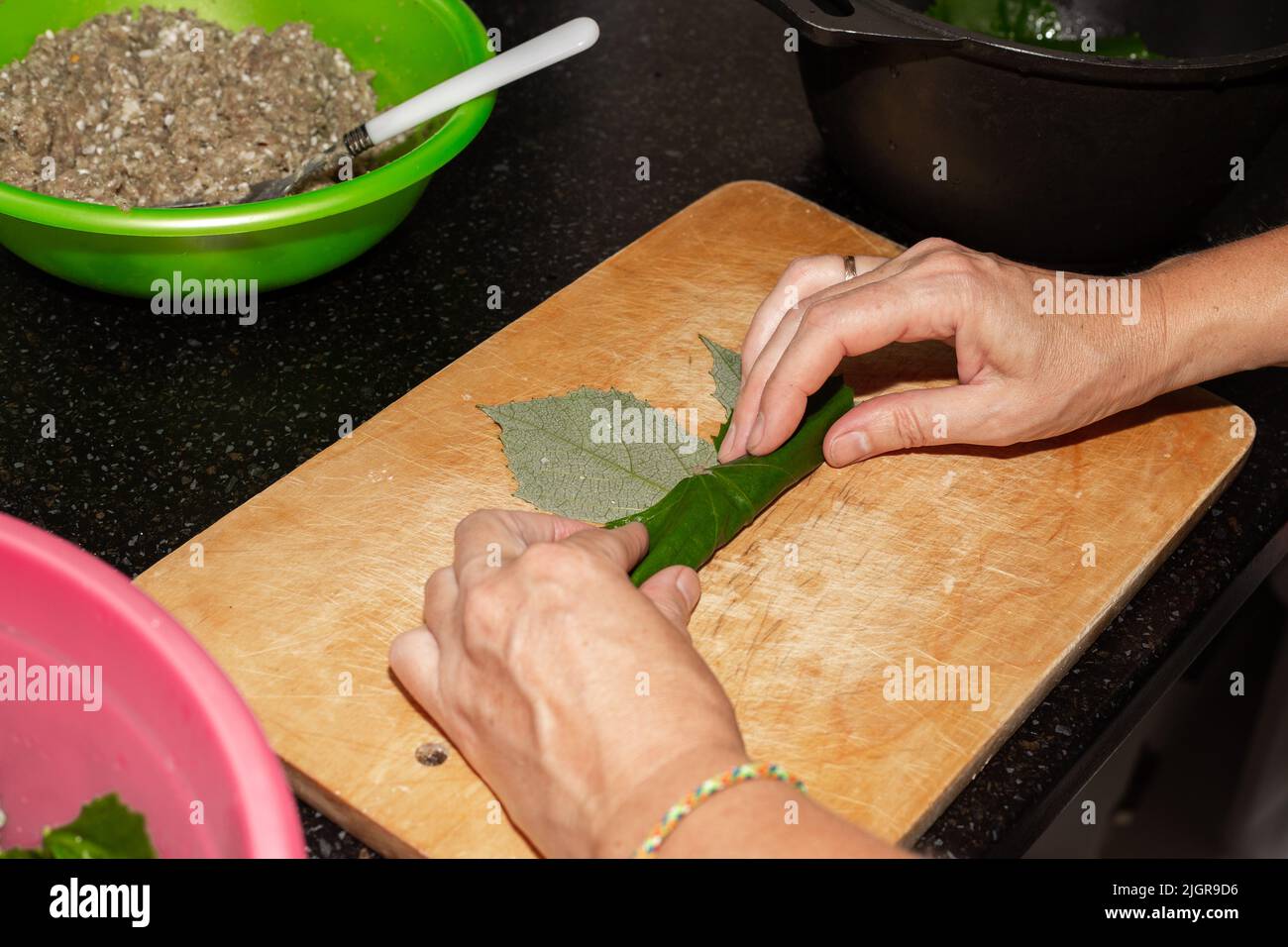 Una donna prepara il cibo a casa. La carne macinata è avvolta in foglie d'uva su un asse di legno, dolma. Foto Stock
