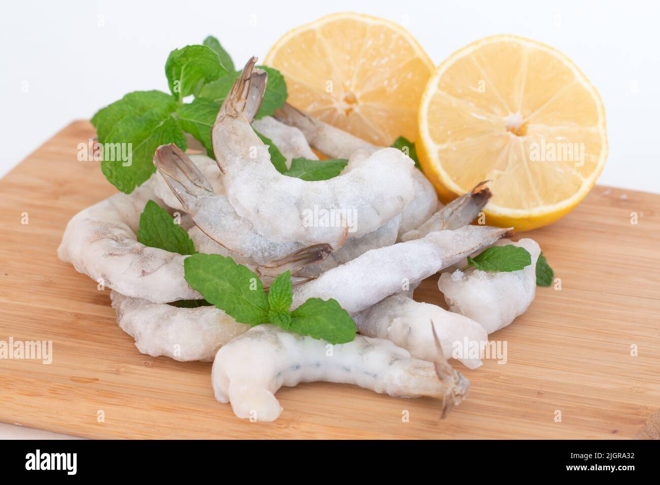 Gamberetti crudi congelati sbucciati su un tagliere di legno con erbe e limone. Foto Stock