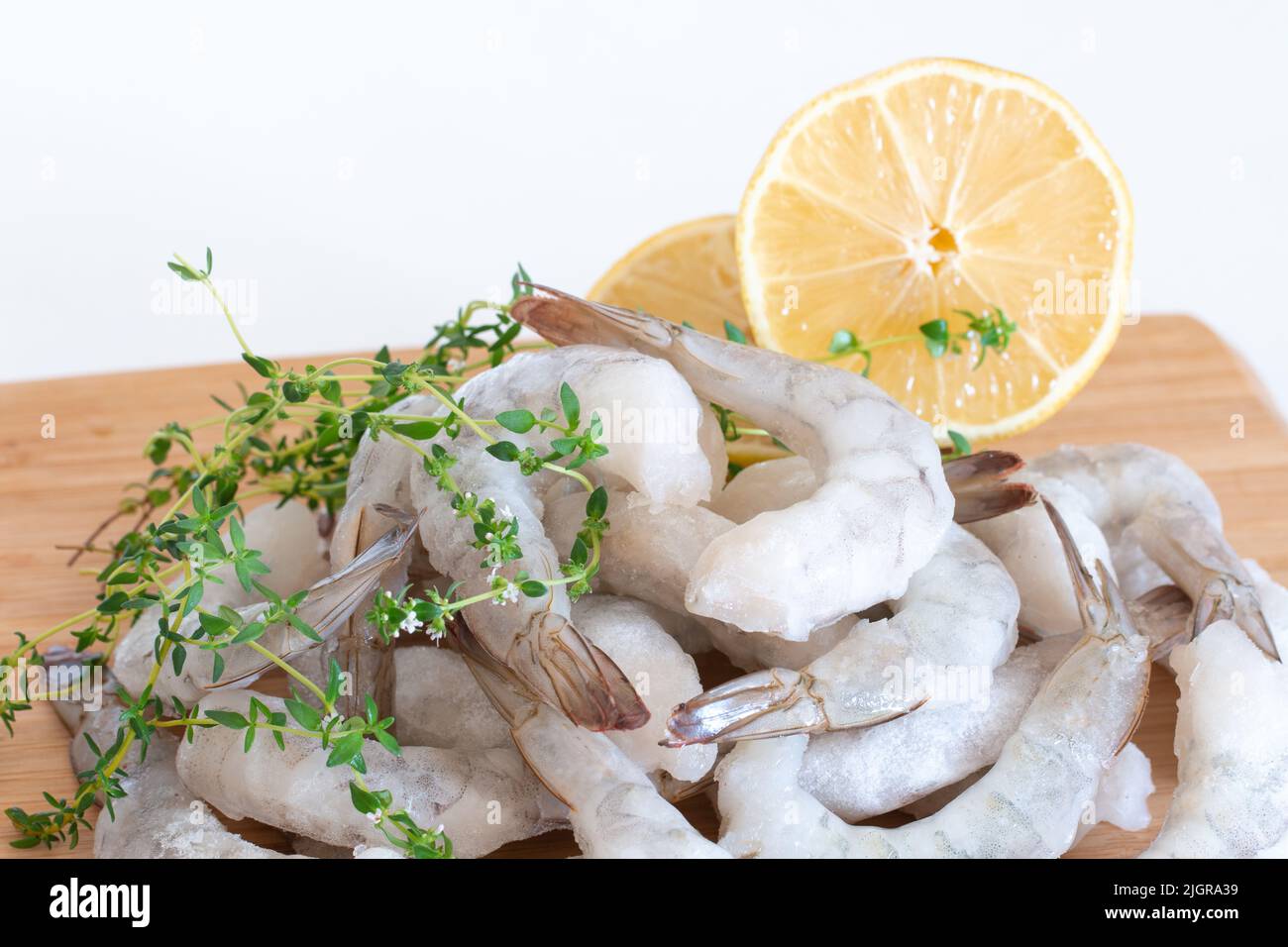 Gamberetti crudi congelati sbucciati su un tagliere di legno con erbe e limone. Foto Stock