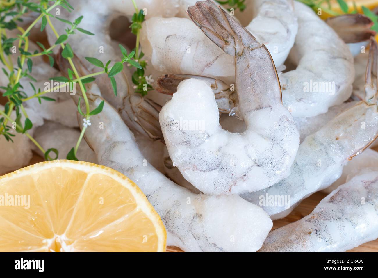 Gamberetti crudi congelati sbucciati su un tagliere di legno con erbe e limone. Foto Stock