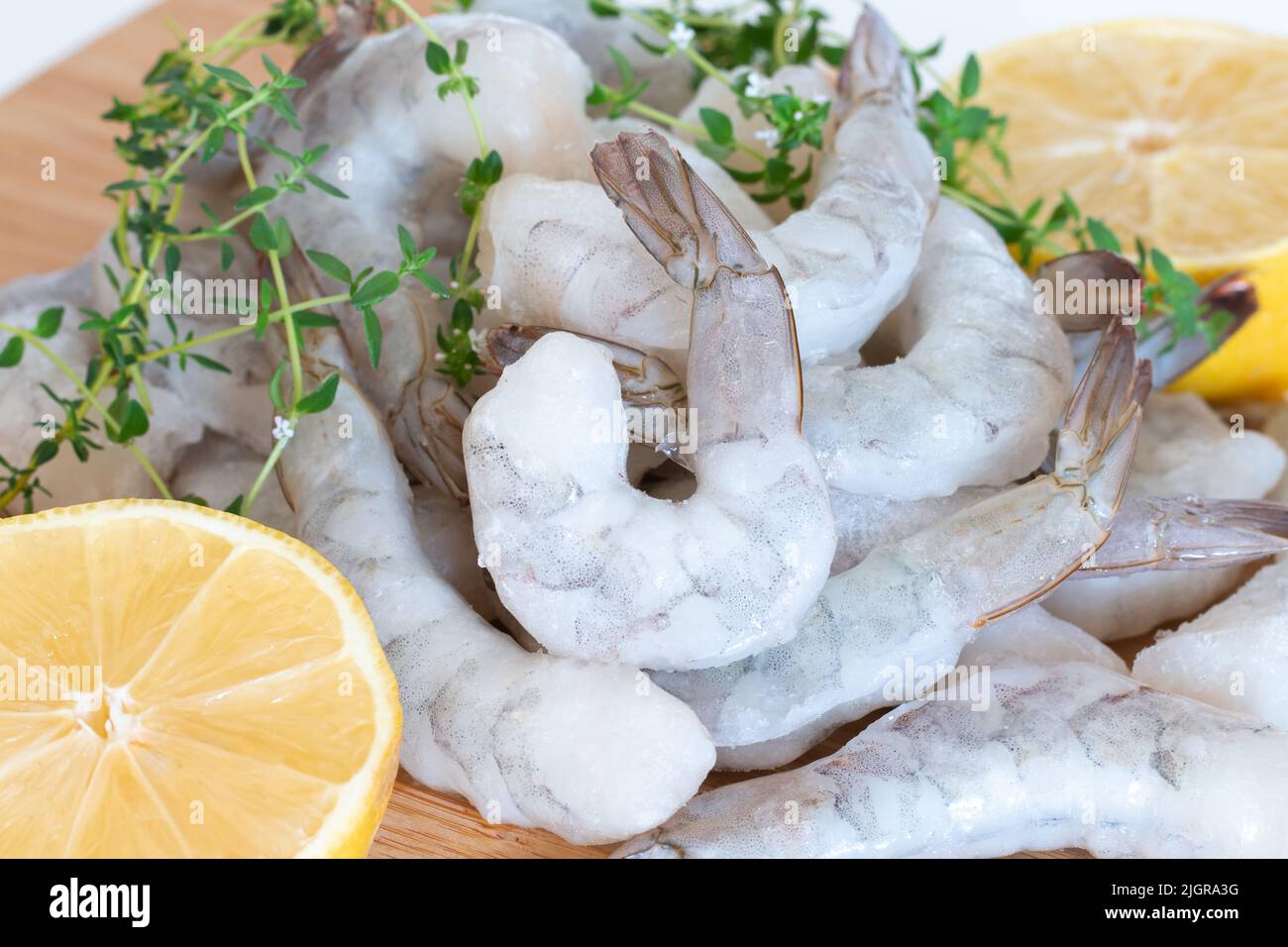 Gamberetti crudi congelati sbucciati su un tagliere di legno con erbe e limone. Foto Stock
