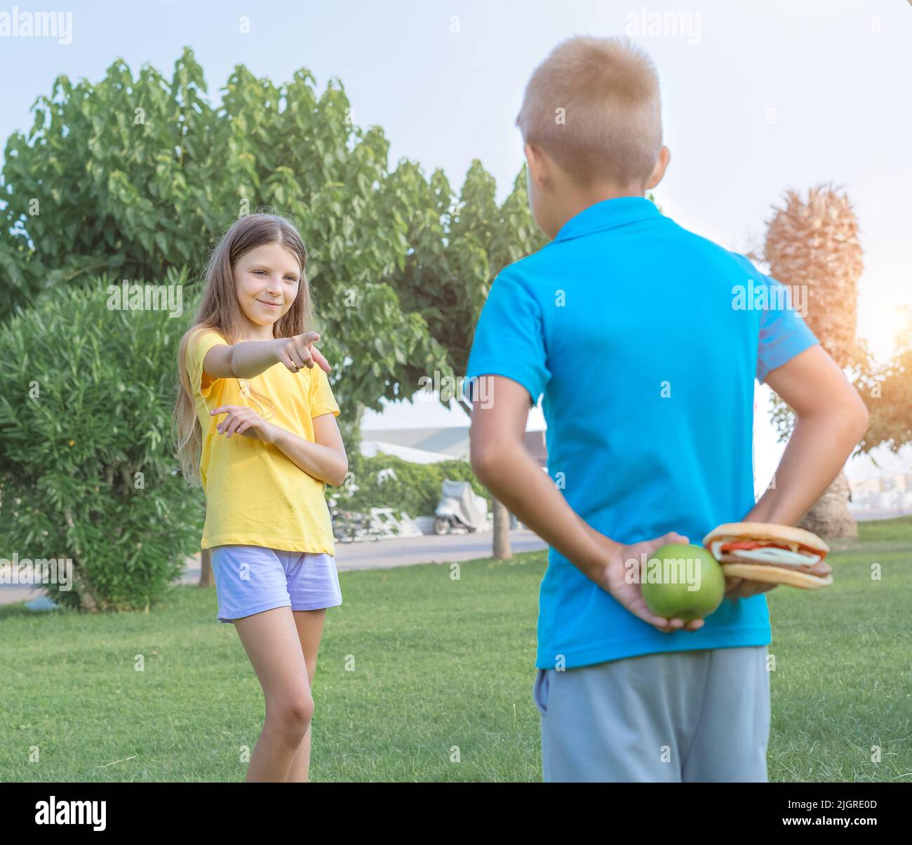 Ragazzo e ragazza adolescenti con mela e hamburger nel parco. Scelta tra cibo sano e malsano. Foto Stock