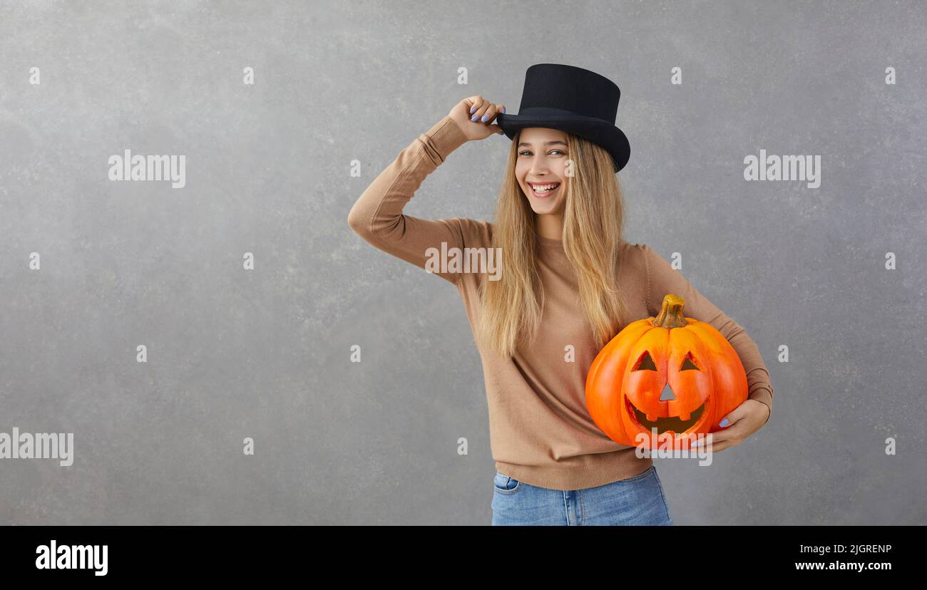 Donna felice in cima cappello che tiene Halloween zucca in piedi su sfondo grigio spazio copia Foto Stock