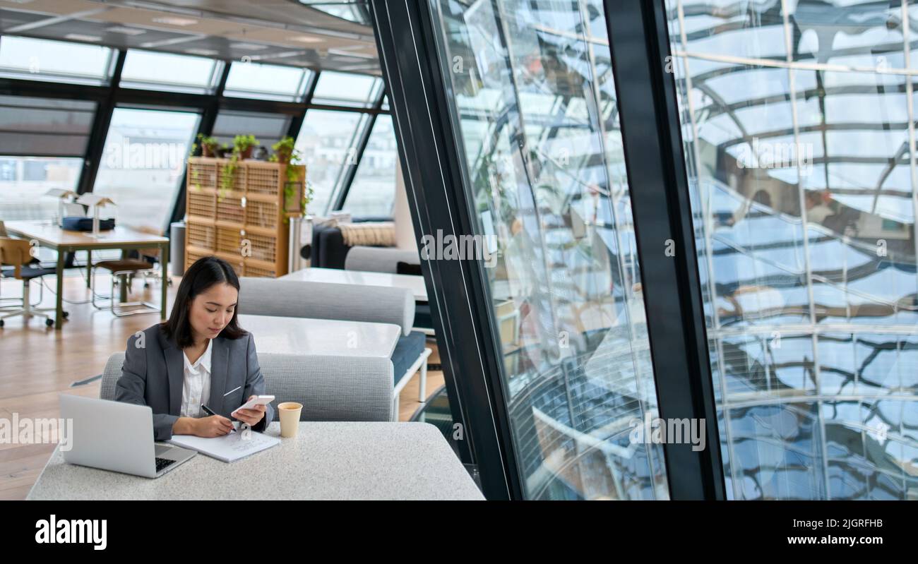 Giovane donna asiatica d'affari che indossa il vestito che lavora in grande ufficio usando il telefono. Foto Stock