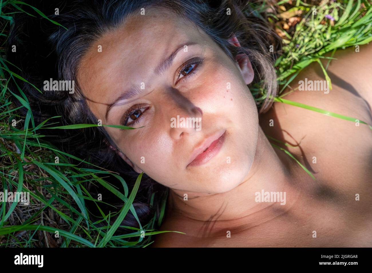 Ritratto di bella, giovane, donna bruna sexy sdraiato in erba di prato estivo in mezzo ombra. Foto Stock