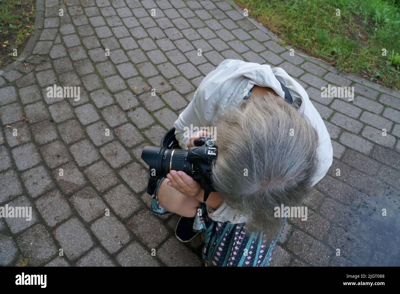 Fotografo in azione. Signora con una fotocamera alla ricerca di una scena per una foto. La fotografia come hobby, passione e professione della gente. Foto Stock