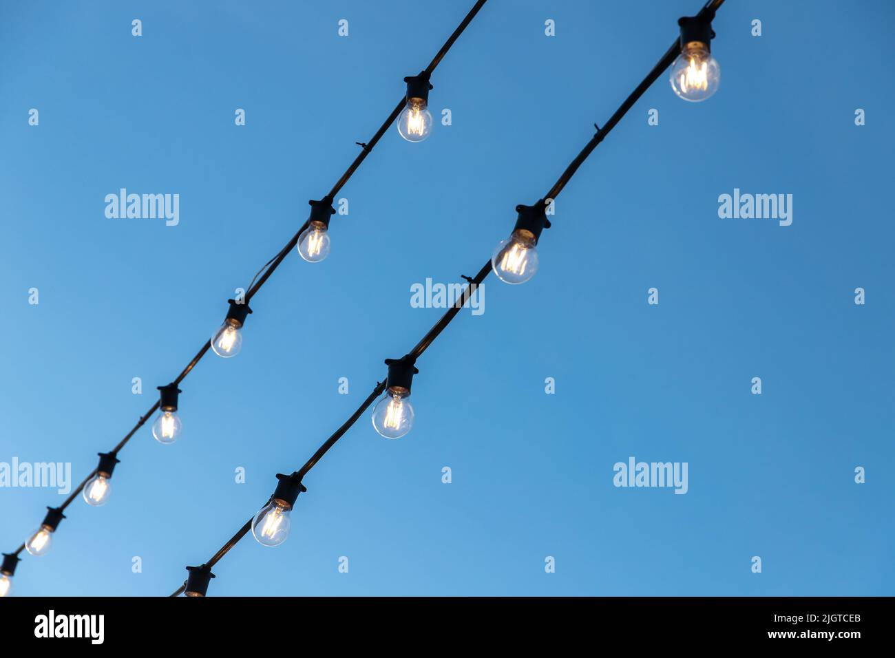 La ghirlanda di lampadine che pende sui cavi neri è sotto il cielo blu della sera Foto Stock