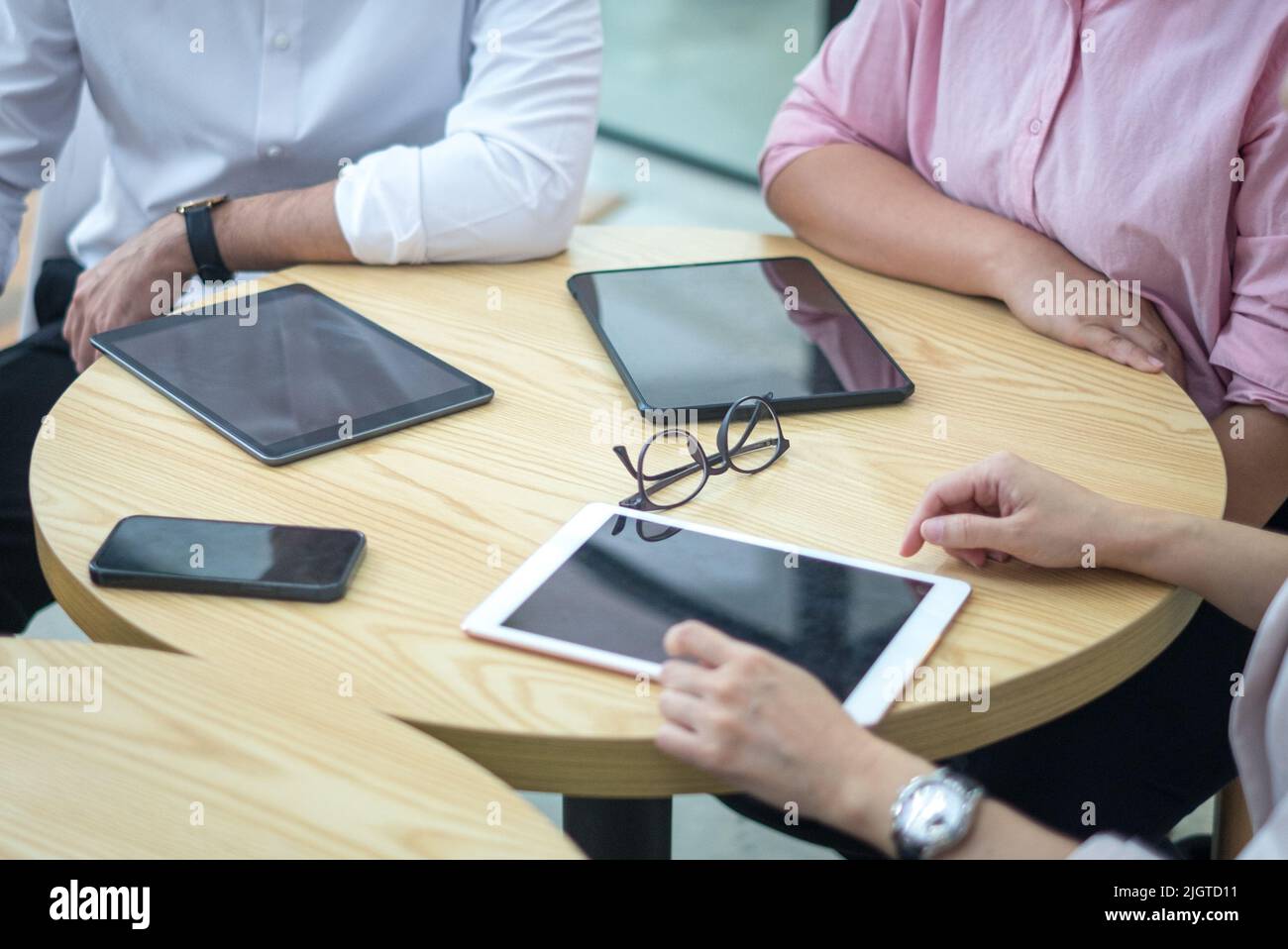 Tablet digitali e smartphone su un tavolo rotondo con persone in viaggio d'affari. Vista dall'alto e da vicino. Foto Stock