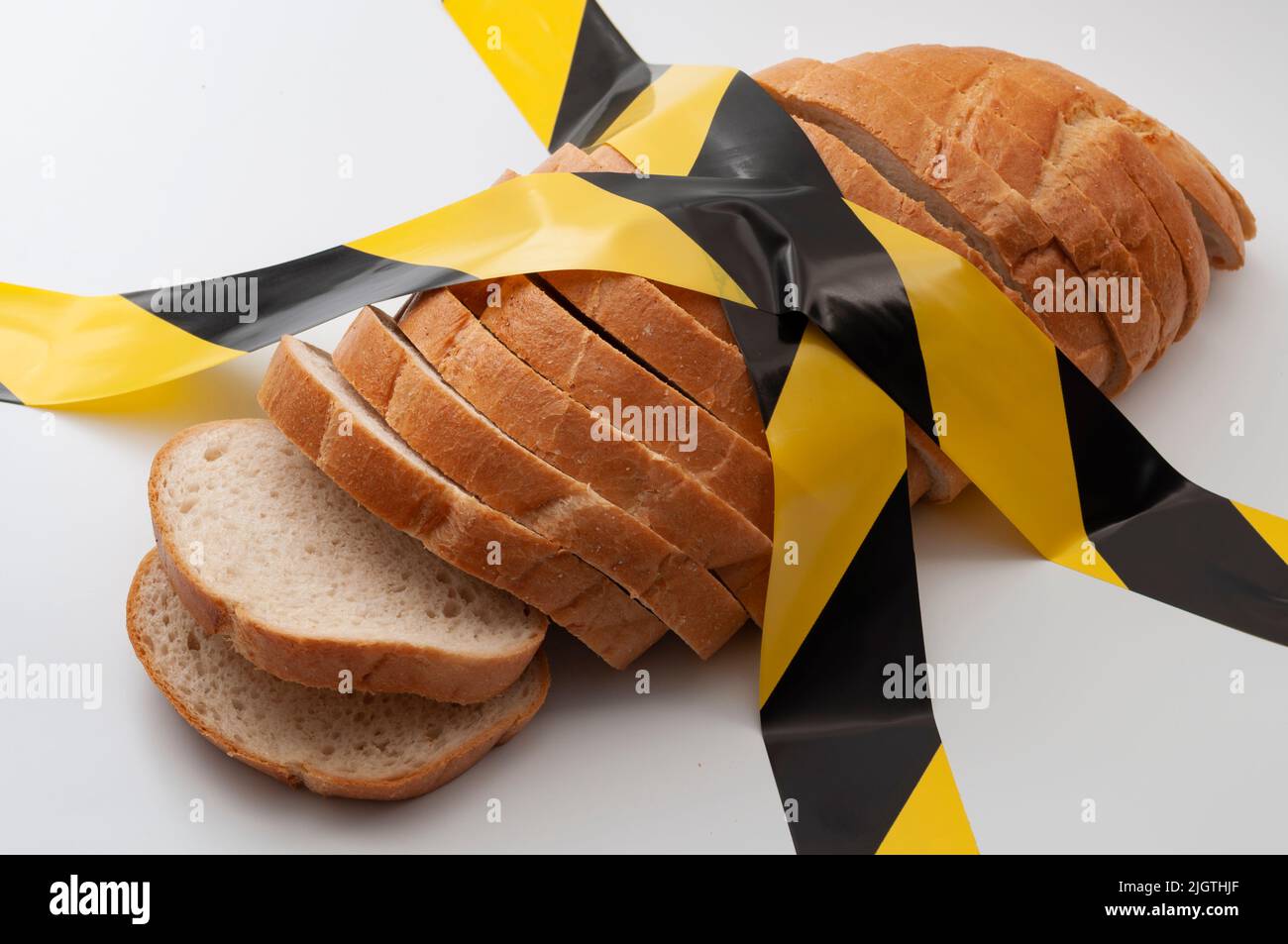 Pane affettato e nastro giallo di attenzione isolato su fondo bianco concetto per l'insicurezza alimentare, avvertimento di fame e cereali lavorati pericolosi Foto Stock