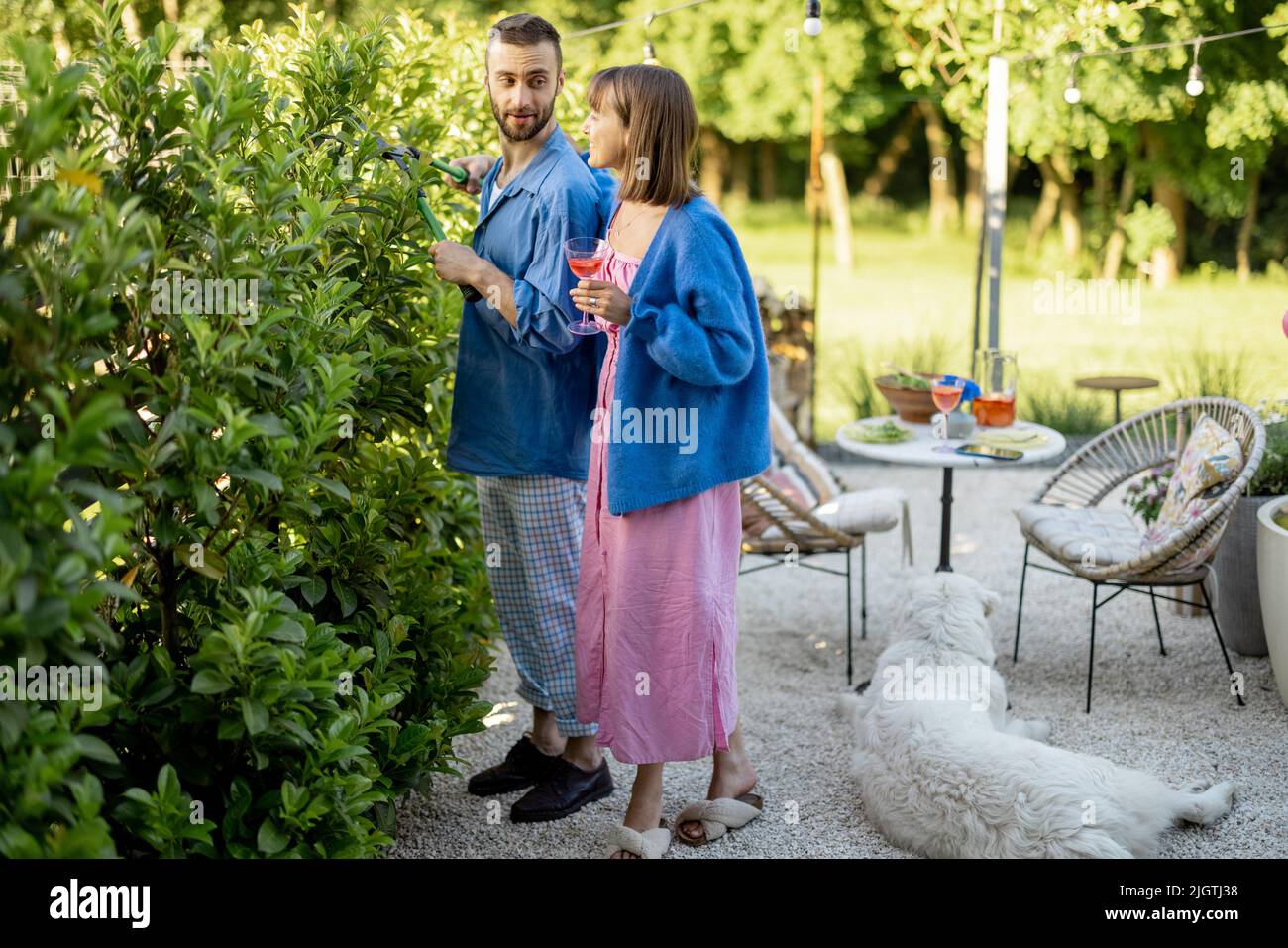 La giovane famiglia passa il tempo estivo, potando cespugli nel cortile della casa di campagna Foto Stock