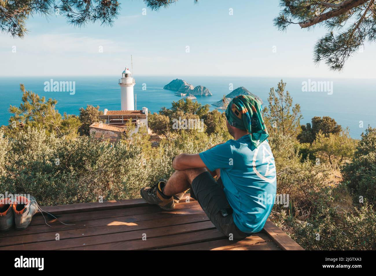 Il viaggiatore siede sullo sfondo di un pittoresco paesaggio marino con piccole isole e un vecchio faro bianco sulla penisola. Un giovane è trekking Foto Stock