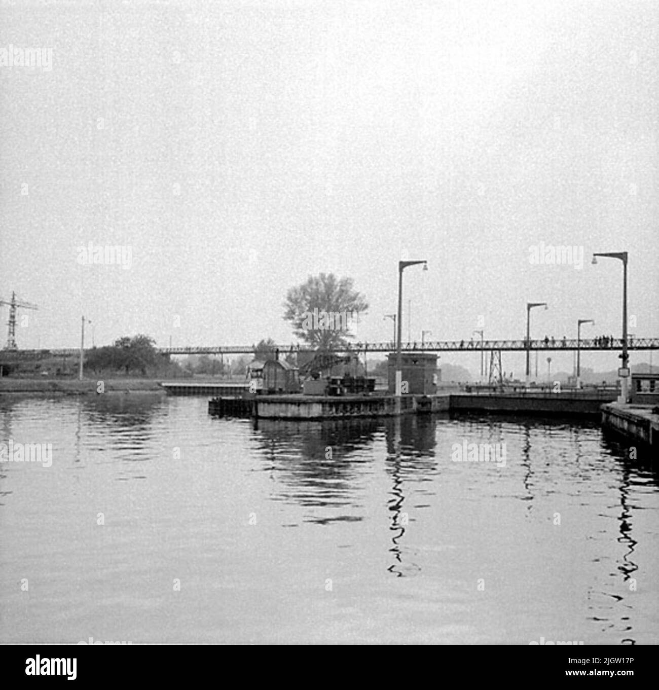 Una serratura in un fiume. Si vede l'ingresso e un cancello. Sopra Slussen va un ponte pedonale, con un certo numero di persone che guardano Slussen. Foto Stock
