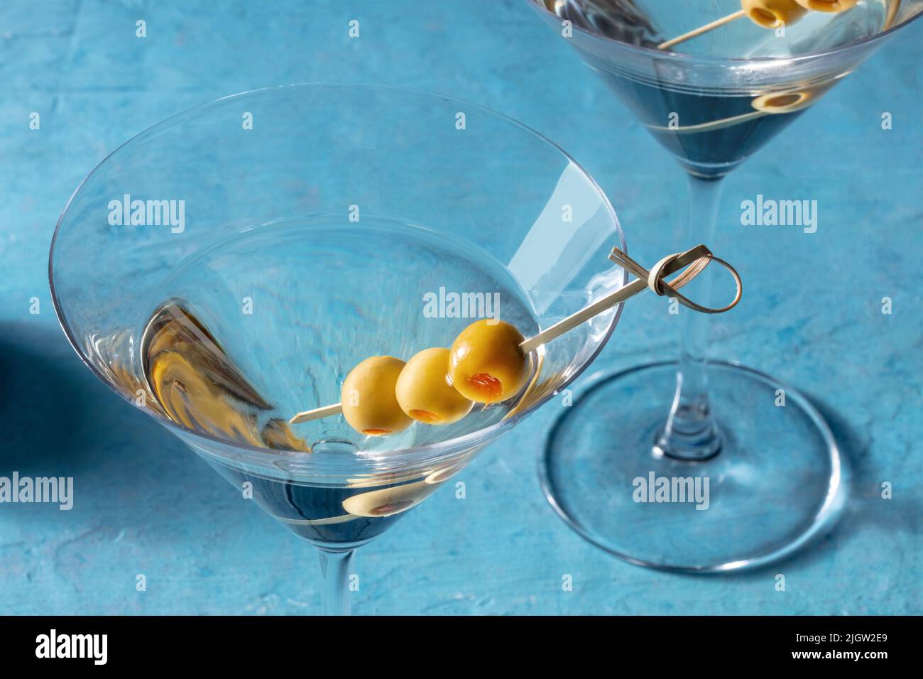 Martini, due bicchieri con olive speziate, su sfondo blu. Primo piano cocktail alcolici Foto Stock