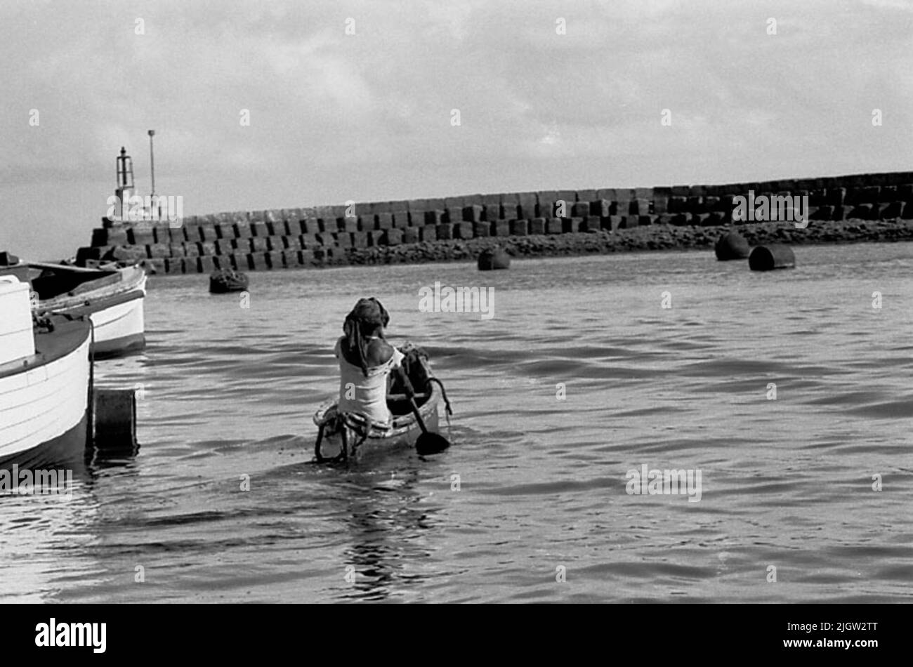 African journey, zanzibars acquisizione semplice: Libri e materiale di archivio.35 immagini in serie. La foto è stata scattata intorno al 1961-09-12. Una donna pagaia una canoa in un porto. A sinistra ci sono alcune barche da pesca ormeggiate. Sullo sfondo un molo si staglia sul mare Foto Stock