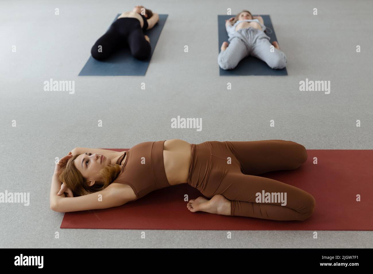 Giovane donna snella sdraiata in Supta Virasana, posa di Hero reclinata, muscoli addominali e posteriori stretching su tappeto in palestra Foto Stock