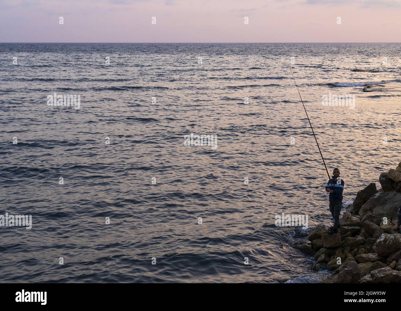 Uomo che pesca al tramonto dalla riva del mare, Governatorato del Nord, Tripoli, Libano Foto Stock