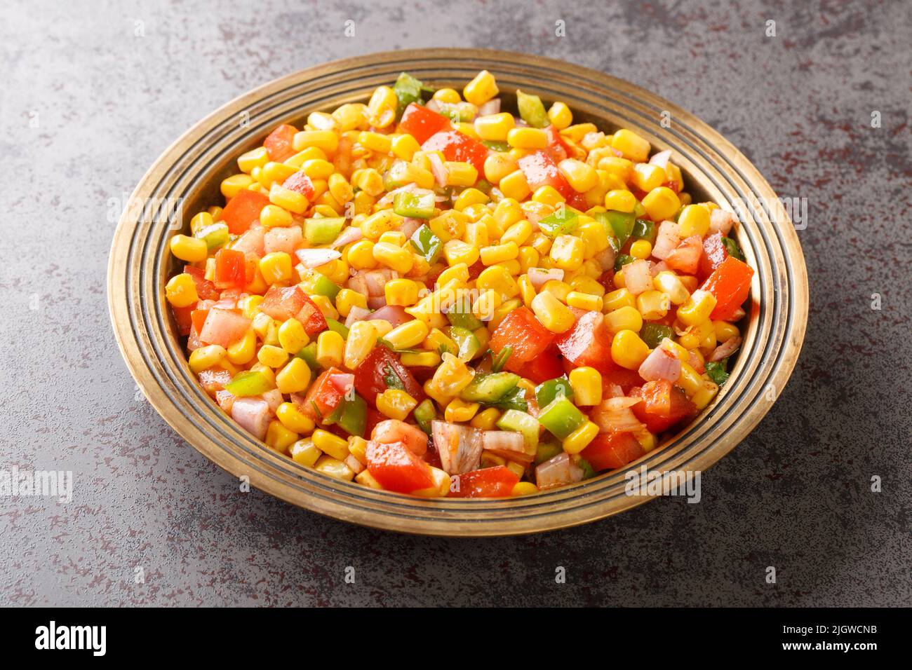 Il mais chaat è uno spuntino super veloce preparato con mais bollito, chaat masala, polvere di spezie, cipolle e pomodori su un piatto di primo piano sul tavolo. Orizzontale Foto Stock